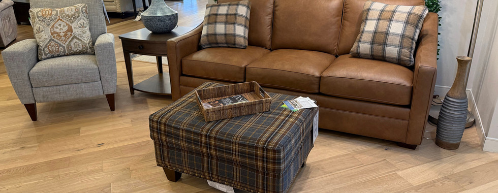 Pairing a rich brown leather sofa with a patterned plaid ottoman creates a warm, layered look.