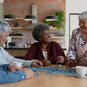 Adults in a supportive shared living environment sitting together at a table, working on a puzzle, drinking coffee, and enjoying community time.