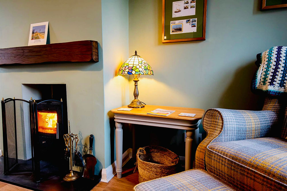Cosy lounge with lit wood-burning stove, and comfortable armchair.