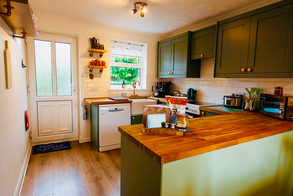 Bright kitchen with green cabinets, wood counters, and white door.