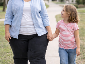 A woman, possibly experiencing lymphedema from hormonal changes, enjoys a walk with a young girl, both savoring a joyful and connected moment on a sunny day.