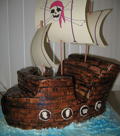 A cake shaped and decorated like a pirate ship with licorice cannons and paper sails
