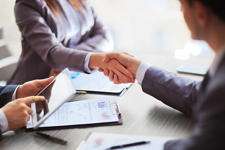 A man and a woman in business suits shaking hands over paperwork
