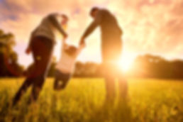 Husband, wife, and young daughter playing in a field with the sunset in the background