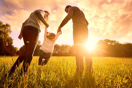 Husband, wife, and young daughter playing in a field with the sunset in the background