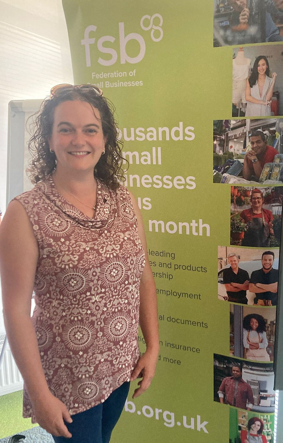 Smiling woman (Hannah) standing in front of a green Federation of Small Businesses (FSB) banner at a networking event in Chichester