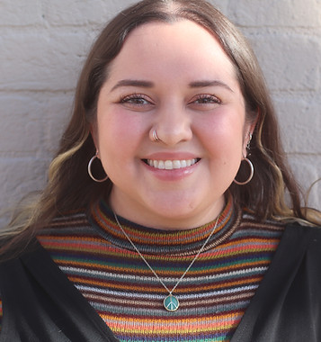 Young woman smiling, dark hair, striped top, turquoise necklace, brick background.