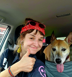 Smiling woman gives thumbs up beside her tan dog in a car.