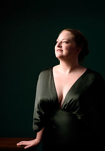 Portrait of Renee Macdonald in an olive green gown against a dark, shadowy background.