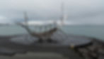 Metallic sculpture of a Viking ship on a stone platform by the sea. Overcast sky and calm water in the background, creating a tranquil mood. Reykjavik, Iceland