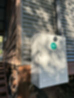 Metal box with green "PV DP" sticker on a building's wooden and metal siding, in a wooded area. Shadows and sunlight create patterns.