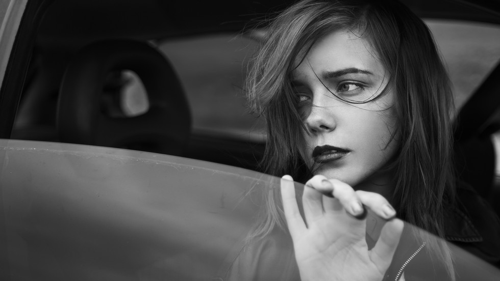 Girl looking out a car window looking at what is behind her with sad expression on her face.