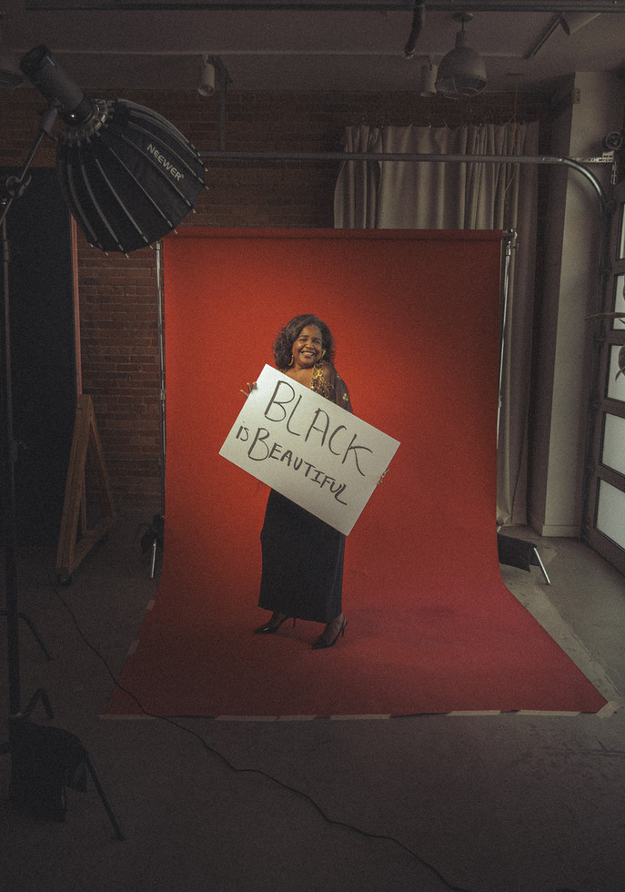 Black women holding a Black is beautiful sign in front of red background