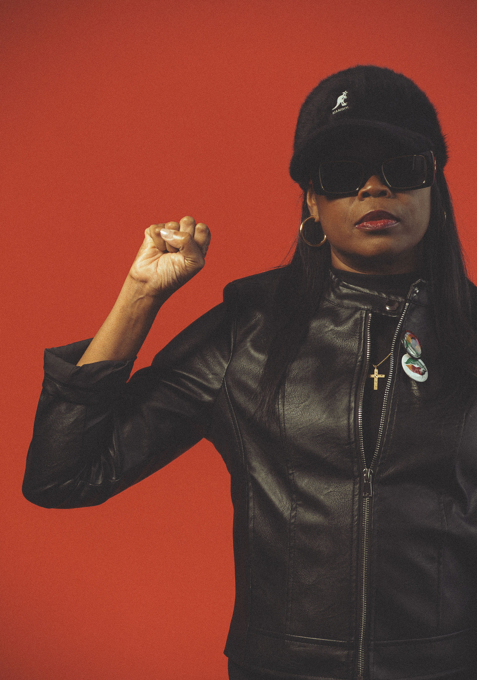 Black women wearing all black with fist in air, infront of red backdrop