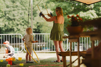 A performer teaches a child how to do tricks by flipping a stick in the air between two held sticks.