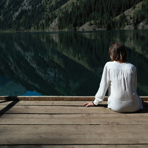 A woman sitting quietly by a still mountain lake, symbolising balance and calm — representing the 40-hour teacher work week in Australia.