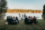 Outdoor wedding at Smoke Signals by Mirror Lake in Lake Placid. couple stands with officiant, guests seated on grass. Sunny day with trees in the background.