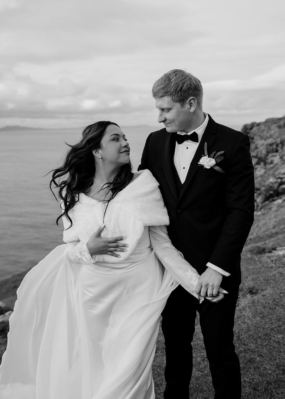 A black and white image of a bride and groom looking lovingly at each other, with the ocean in the background.