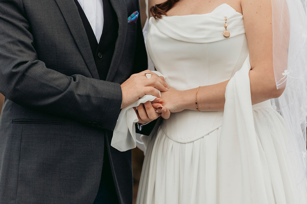 Bride and groom holding hands during a wedding ceremony, her white dress and veil beside his dark suit, intimate and joyful