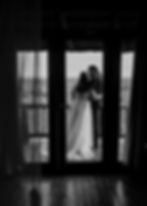 Couple embracing on a wooden balcony, overlooking a vast landscape. The woman wears a lace gown. The scene is in black and white, evoking romance.