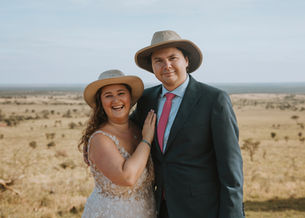 A bride and groom wear safari hats in front of the savannah in the Serengeti