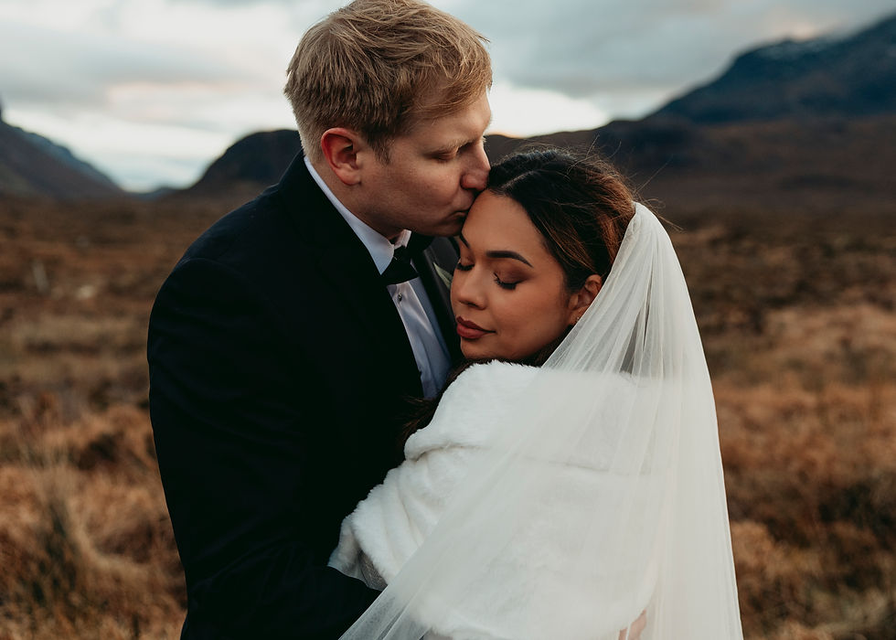 A close up image of a groom kissing a bride on her forehead while she smiles slightly. Her eyes are closed. 