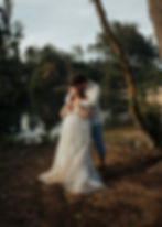 A couple embraces by a tropical Hawaiian beach. The bride in a white lace dress. The scene evokes romance and tranquility.