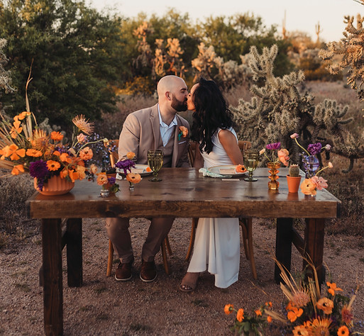 bride and groom kissing over a set dinner table with beautiful floral arrangements, and the Arizona desert in the background