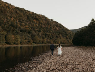 A bride a groom walk alongside a river with mountains in the background on their elopement day