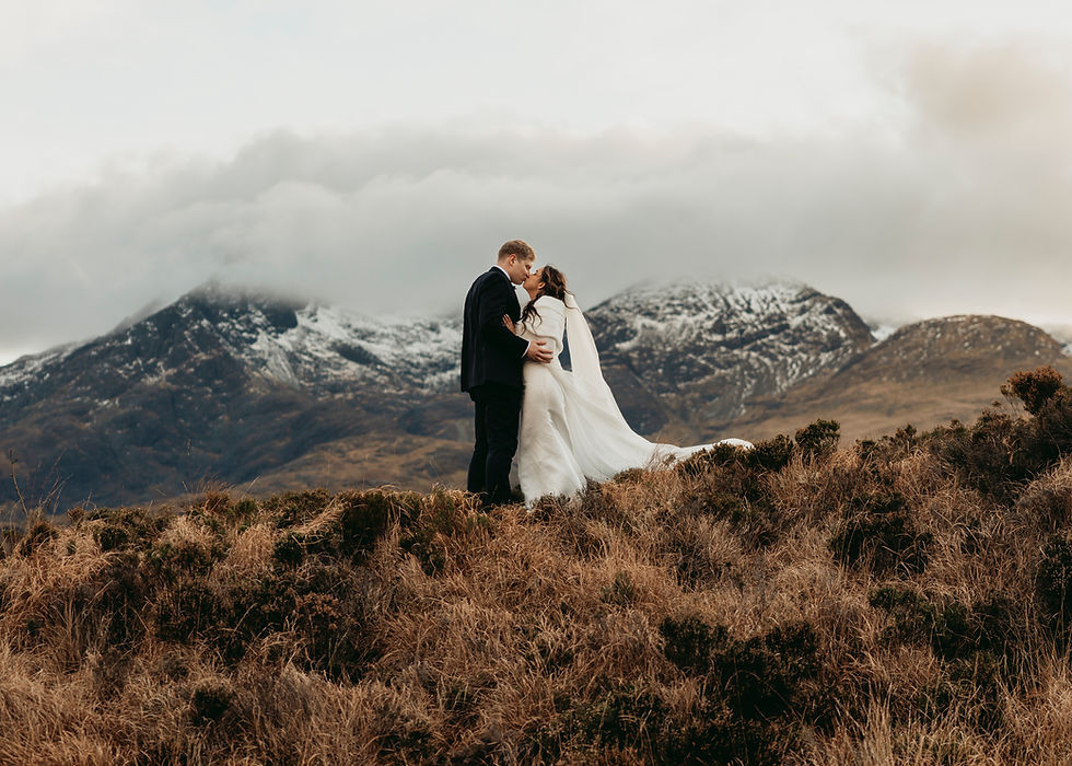 A bride and groom kiss on top of a hill with snowy mountains in the background. 