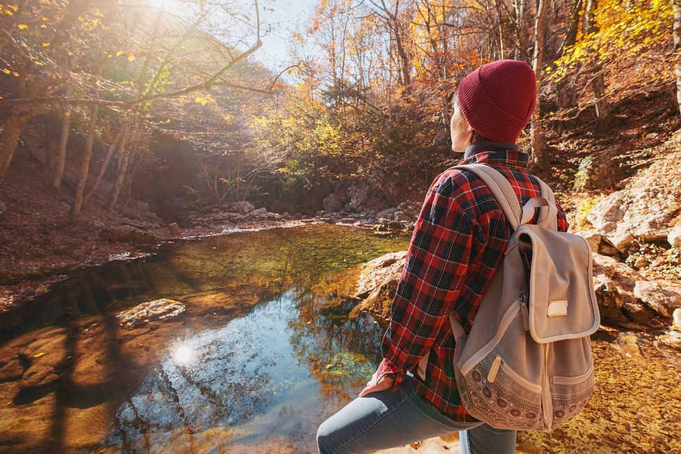 Hiker in a red plaid shirt overlooks a small pond in the autumn woods in Vermont