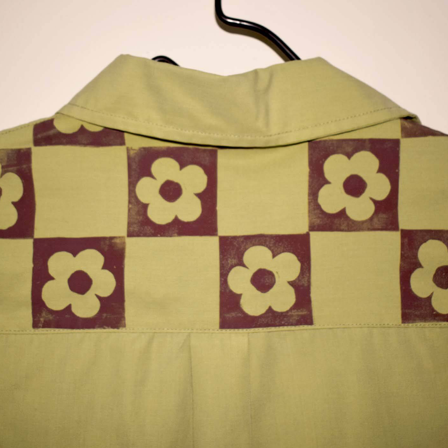 Up close view of a green sleeveless shirt showing checkerboard pattern with flower motifs across shoulder yoke.