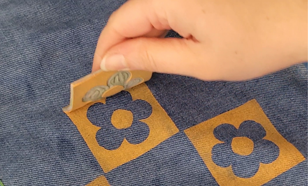 Hand peeling an orange flower-shaped lino print from blue patterned fabric creating a floral checkered pattern.