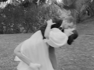 Bride and groom share a joyful kiss in a garden, with blurred motion capturing their dance. Trees and greenery create a romantic backdrop.