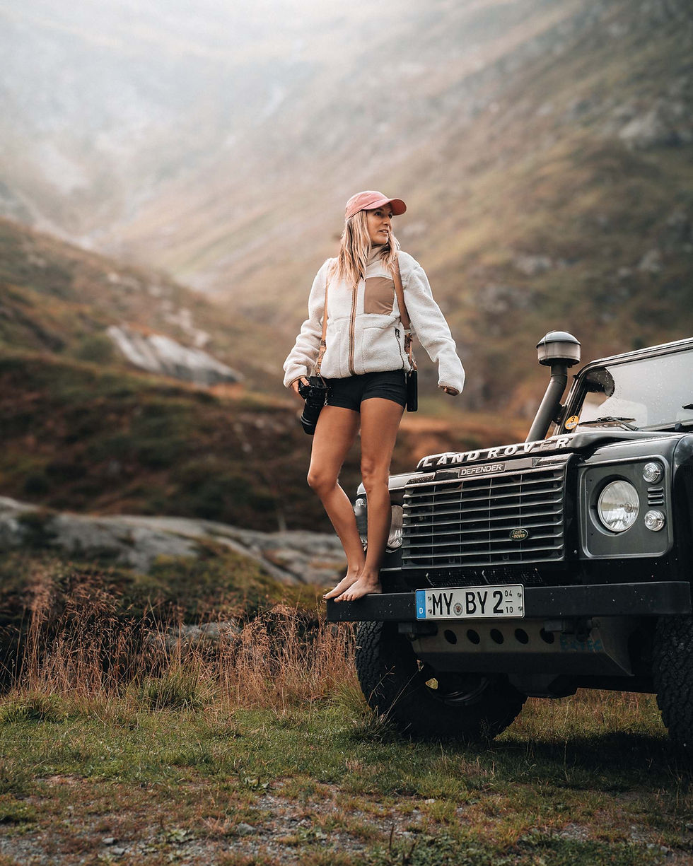 Christine Bay, travel and wildlife photographer, standing on her Land Rover Defender in misty mountains