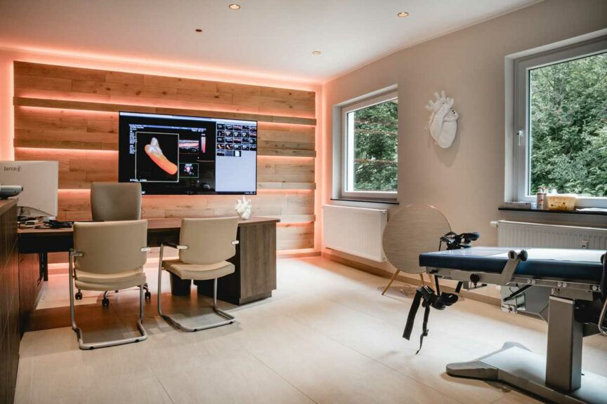 Foto des Behandlungsraums der Praxis mit Schreibtisch, Monitor und Behandlungsliege