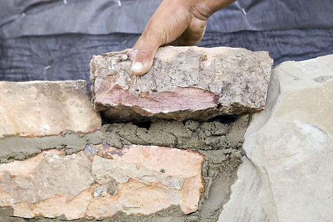 Someone using their hands to build a brick wall using cement.