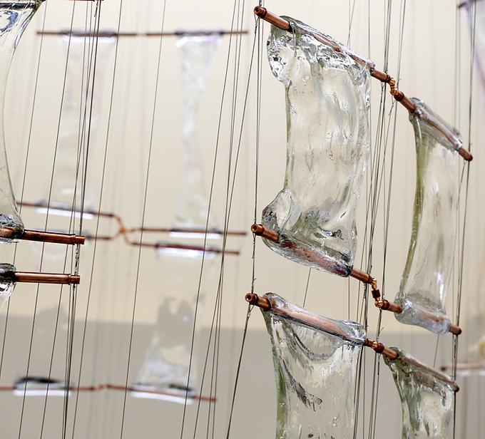Curator Jocelyne Prince has brought together five artists: Justin Ginsberg, Romina Gonzales, Ashley Raye Harris, Matthew Day Perez, and Alexander Wenstrup, who have an acute understanding of how just a few millimeters of glass can shift our perception of the world. Each work in this exhibition catalyzes the optical and sculptural space that exists within a sheet of glass. In some cases, the surface of the glass has been disrupted, or bears the marks of the action of its making, or the glass composition has been specially concocted to refract light, or the tiniest amount of air is trapped and visually manifested. A fascination with surface, the space just beyond the surface, what we see through the glass, the space within the glass, and what we see reflected in the glass preoccupies these artists.
The works in this exhibition have been selected in conjunction with, and as a complement to the research and activities that are part of the November 2026 WheatonArts symposium on window glass production methods, “Transparent Thresholds.”