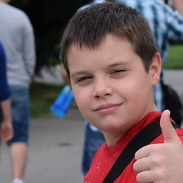 boy with red T-shirt and rucksack giving a thumbs up.