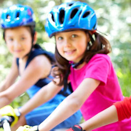 3 smiling children with helmets, on bikes.