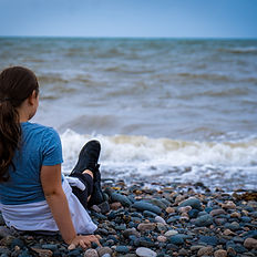 Woman sits oceanside, gazing at waves
