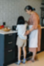 child and adult standing in front of stove cooking