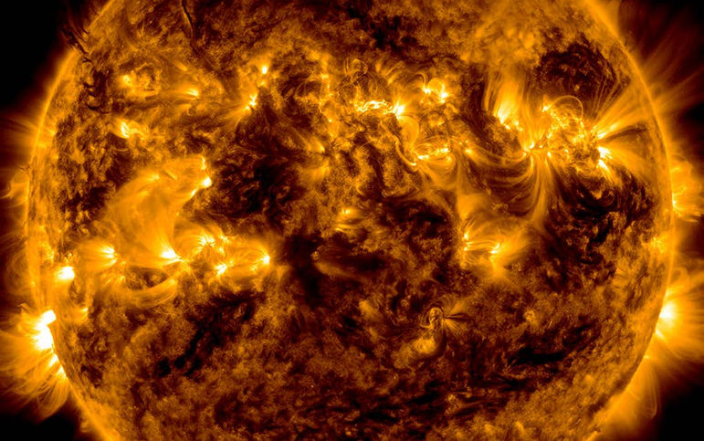 Vue complète du Soleil en teintes jaunes et dorées, montrant de nombreuses régions actives brillantes réparties sur sa surface. Des boucles de plasma s’élèvent autour de ces zones, révélant une activité magnétique intense. 
