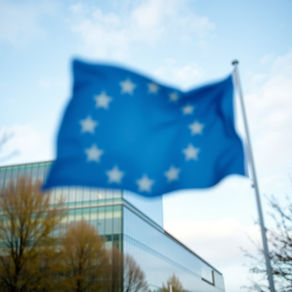 An EU flag blurred in the background with a modern glass office building in sharp focus, representing Ireland’s strategic shift in AI governance within the European regulatory landscape.