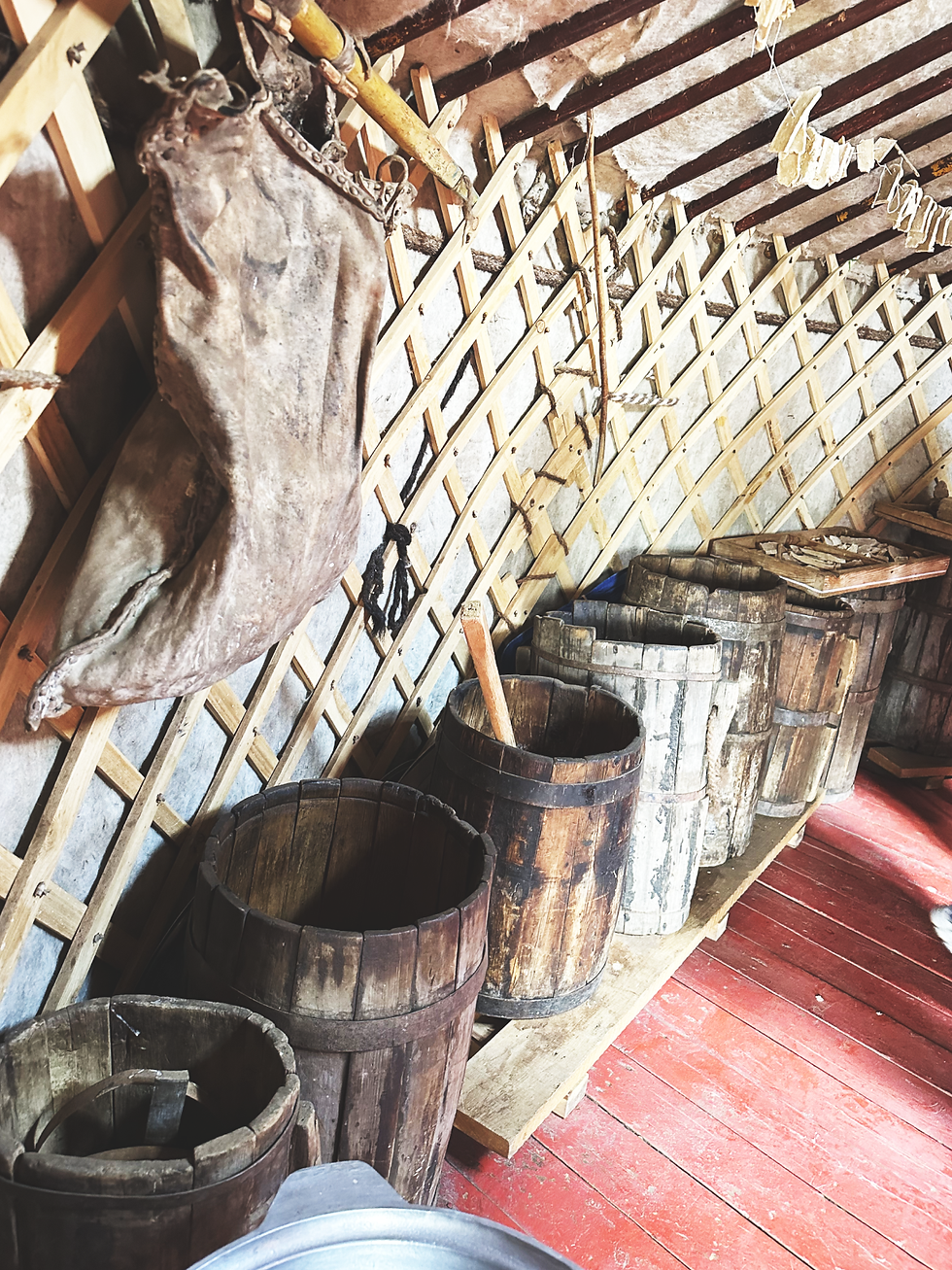 Wooden barrels line a rustic interior with a wooden lattice wall and red floor. A large sack hangs on the wall, creating an antique feel.