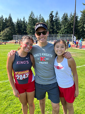 Greg and his two daughters at a sporting field, enjoying time together.