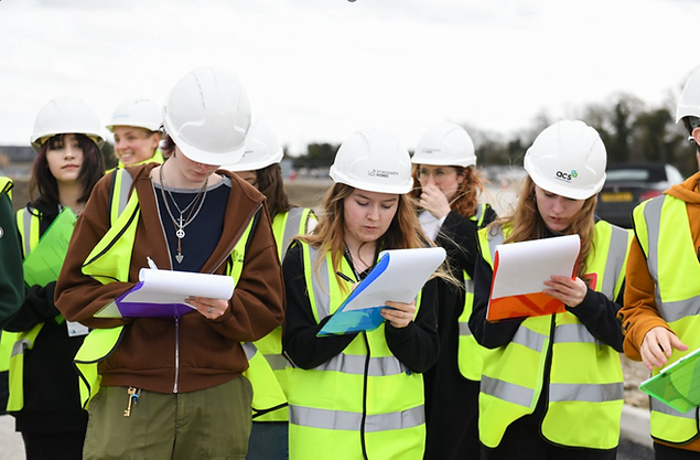 Group of young adults with hard hats and high vis jackets, taking notes in notebooks