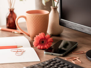 Flat lay of a feminine office desk with coral-toned accessories, fresh flowers, a computer monitor, and a notebook—perfect for a Charlotte-based female entrepreneur working on her marketing and SEO.