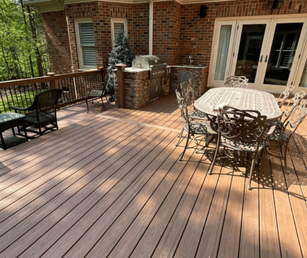 Custom deck with outdoor dining set and grill area behind brick home