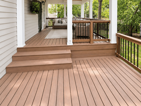Brown backyard deck with wide steps leading to a covered seating area with cushioned furniture, white posts, and black balusters.